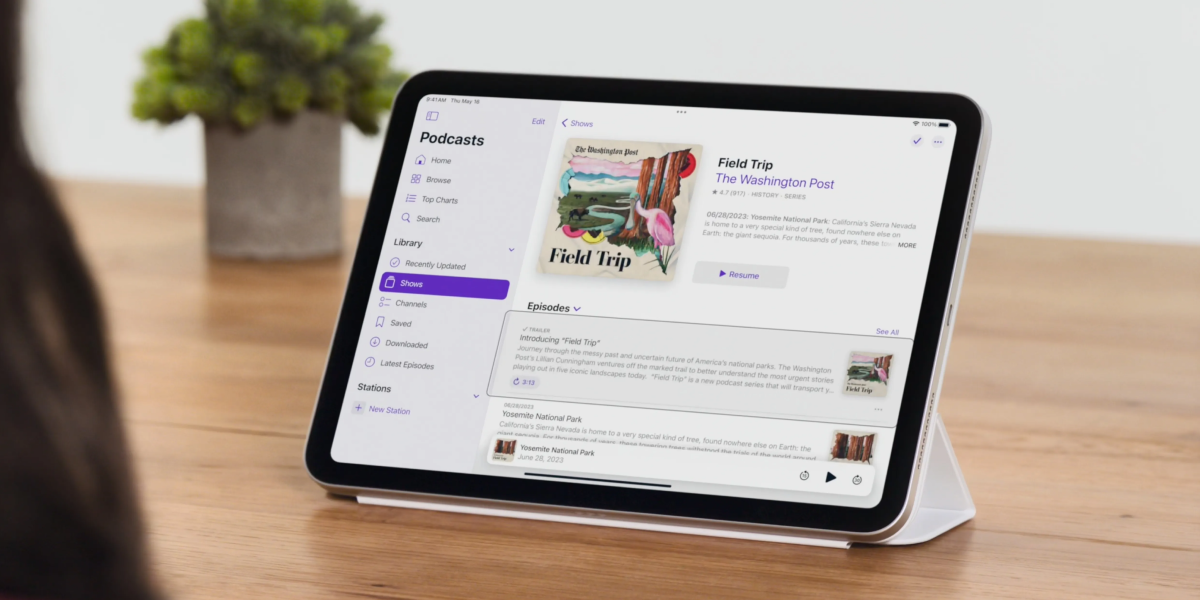 An iPad sitting on a table, propped up by a stand. A podcast episode is being highlighted for selection with eye tracking.